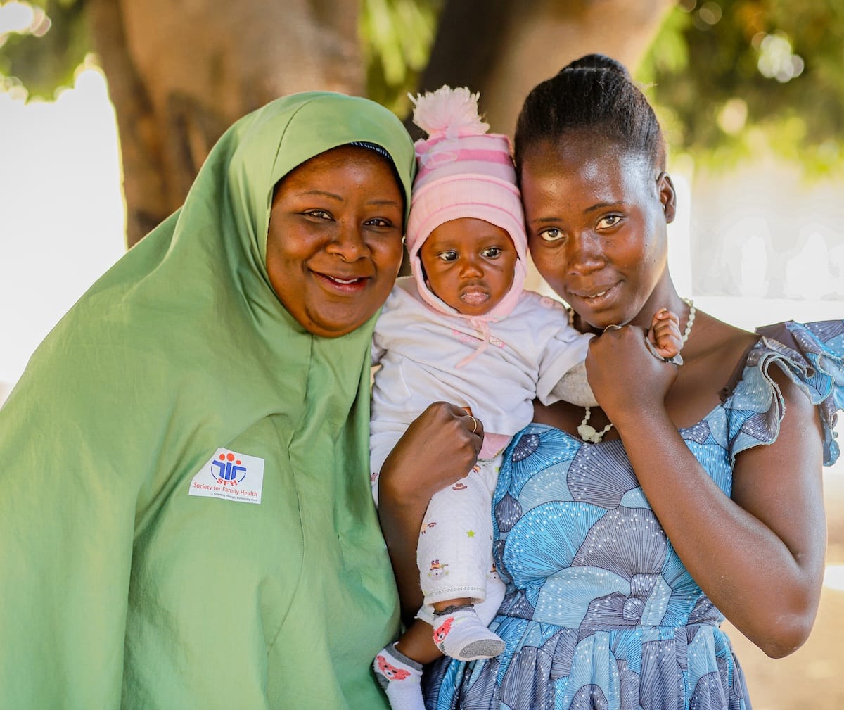 A community health worker stands with a young mother holding her baby