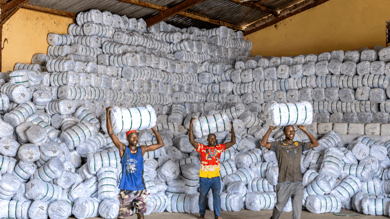Warehouse workers lifting bales of insecticide-treated mosquito nets stacked floor to ceiling, ready for state distribution